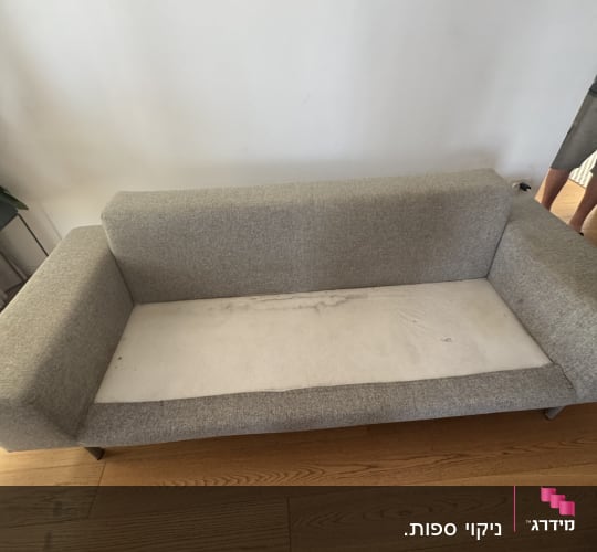 ספה אפורה עם כרית ישיבה מלוכלכת על רצפת עץ
